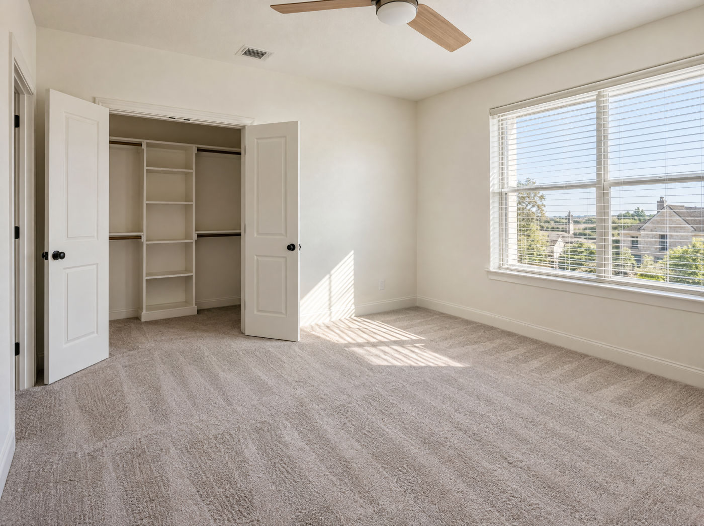 An empty bedroom with clean carpet, wiped baseboards and a dusted ceiling fan